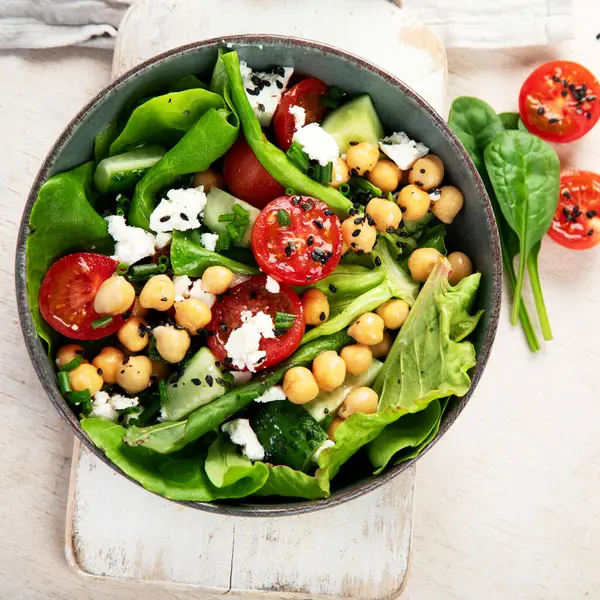 Domates, salatalık, salata, nohut ve peynirli vejetaryen nohut salatası hafif bir arka planda. Sağlıklı bir yaşam tarzı. Üst yaşam