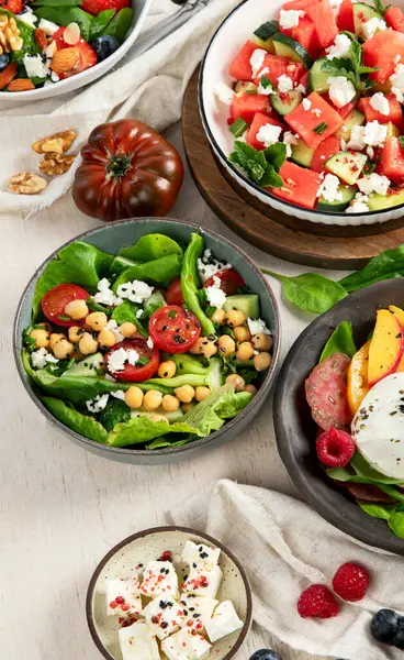 Çilekli çeşitli yaz salataları, otlar. Hafif arkaplanlı sağlıklı salata, şeftali, burrata, yabanmersini ve ceviz. Sağlıklı yemek için taze yararlı yemek. Üst görünüm.