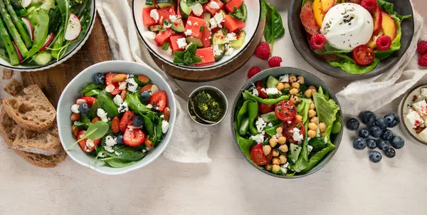 Çilekli çeşitli yaz salataları, otlar. Hafif arkaplanlı sağlıklı salata, şeftali, burrata, yabanmersini ve ceviz. Sağlıklı yemek için taze yararlı yemek. Üst Manzara. Boşluğu kopyala.