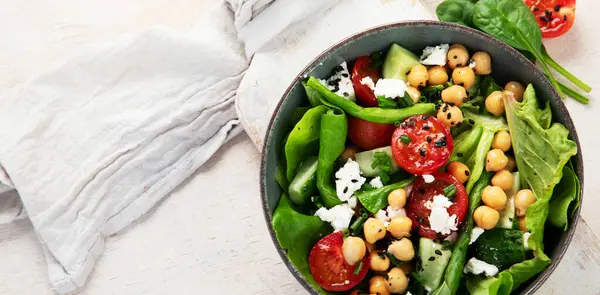 Domates, salatalık, salata, nohut ve peynirli vejetaryen nohut salatası hafif bir arka planda. Sağlıklı bir yaşam tarzı. Üst görünüm, alanı kopyala.