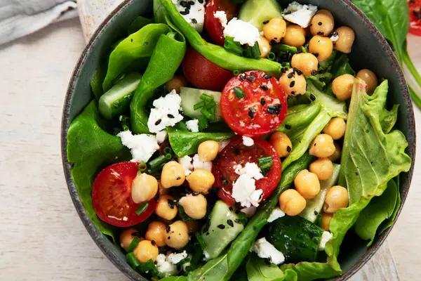 Domates, salatalık, salata, nohut ve peynirli vejetaryen nohut salatası hafif bir arka planda. Sağlıklı bir yaşam tarzı. Üst yaşam