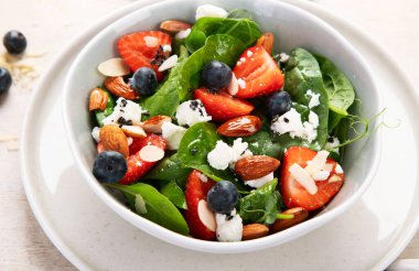 Ispanak ve çilekli yaz salatası süzme peynir ve hafif arka planda badem. Üst görünüm. 