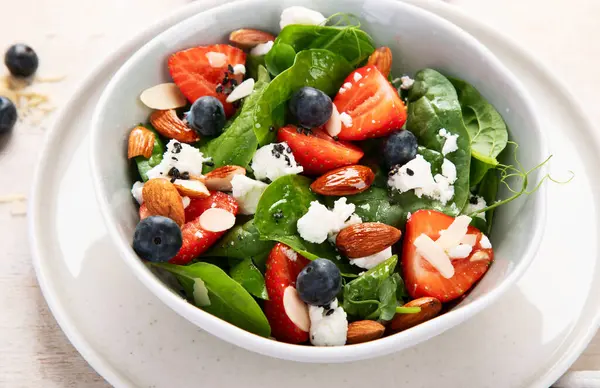 Ispanak ve çilekli yaz salatası süzme peynir ve hafif arka planda badem. Üst görünüm. 