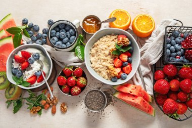 Sağlıklı kahvaltı için organik malzemeler - yoğurt, fındık, taze meyve, yulaf ezmesi, beyaz arka planda tam tahıl gevreği. Üst görünüm.