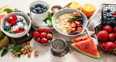 Sağlıklı kahvaltı için organik malzemeler - yoğurt, fındık, taze meyve, yulaf ezmesi, beyaz arka planda tam tahıl gevreği. Üst Manzara. Boşluğu kopyala.