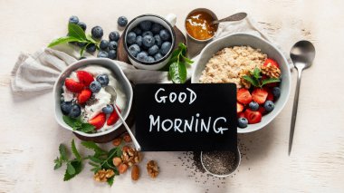 Sağlıklı kahvaltı için organik malzemeler - yoğurt, fındık, taze meyve, yulaf ezmesi, beyaz arka planda tam tahıl gevreği. Üst görünüm.