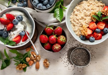 Sağlıklı kahvaltı için organik malzemeler - yoğurt, fındık, taze meyve, yulaf ezmesi, beyaz arka planda tam tahıl gevreği. Üst görünüm.