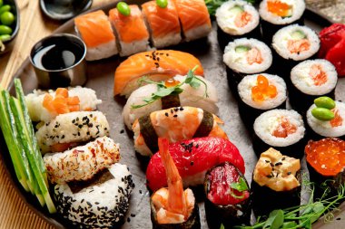 Somon, ton balığı ve sebzeli suşi ruloları bir tabakta servis edilir. Hafif arka planda Asya yemekleri. Üst görünüm.