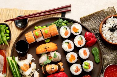 Somon, ton balığı ve sebzeli suşi ruloları bir tabakta servis edilir. Hafif arka planda Asya yemekleri. Üst Manzara. Boşluğu kopyala.