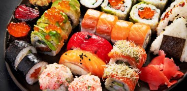 Çeşitli suşi nigiri ve maki büyük set. Ton balıklı, yengeçli, somonlu ve koyu arkaplanda yuvarlanan bir çeşit Japon suşisi. Üst Manzara. Panorama.