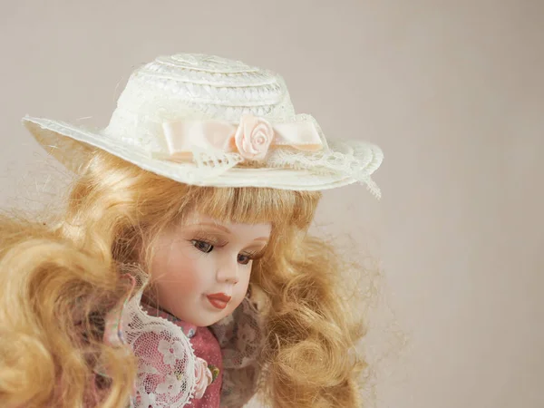 Vintage porcelain doll golden-haired girl with flowing hair with brown eyes in a pink dress and a straw hat