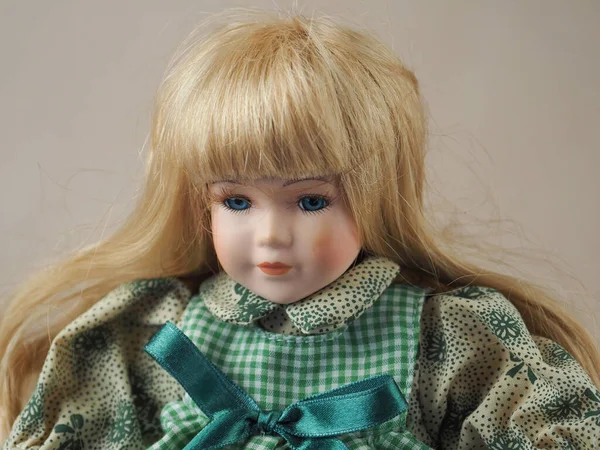 緑のプレイドレスで金色の髪を流れると青い目を持つヴィンテージ磁器人形の女の子 — ストック写真