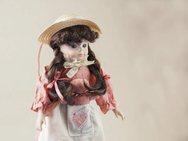 ピンクのドレスに青い目の茶色の組紐とポケットにおもちゃと白いエプロンとヴィンテージ磁器人形の女の子とわら帽子 — ストック写真