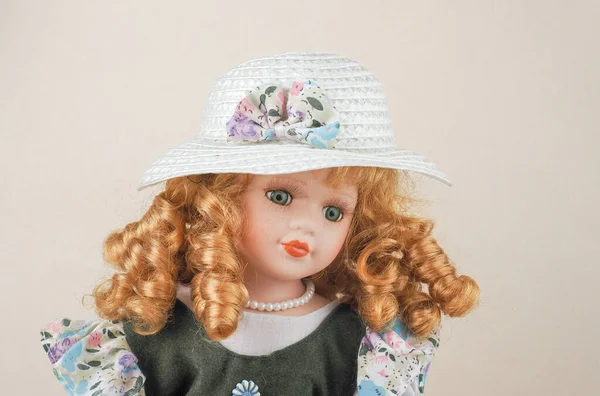 カールを持つヴィンテージ磁器人形緑目の赤髪の女の子 彼女の首の周りの真珠のビーズ 緑のサンドレスと花と白のわらの帽子で — ストック写真