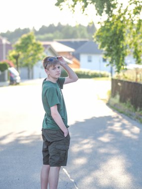 Dost canlısı, mavi gözlü, güneş gözlüklü ve yeşil tişörtlü bir gencin açık hava portresi.