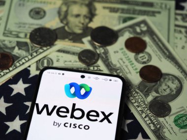 Bavyera, Almanya - 9 Aralık 2023: Bu fotoğraf illüstrasyonunda, Webex Cisco logosu arka planda ABD Doları banknotları ve bozuk paralarla bir akıllı telefonda görüntülenmiştir..