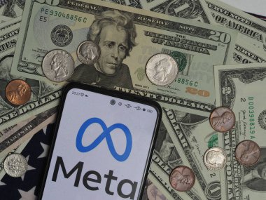 Bavyera, Almanya - 26 Aralık. 2023: Bu resimde, bir Meta Platformları, Inc. logosu arka planda ABD Doları banknotları ve bozuk paralarla bir akıllı telefonda gösteriliyor. 