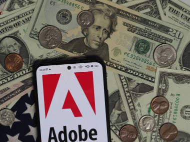 Bavyera, Almanya - 26 Aralık. 2023: Bu resimde Adobe Inc. logosu, arka planda ABD Doları banknotları ve bozuk paralarla akıllı bir telefonda sergileniyor. 