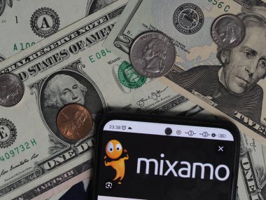 Bavyera, Almanya - 26 Aralık. 2023: Bu resimde, bir Mixamo Inc. logosu arka planda ABD Doları banknotları ve bozuk paralarla akıllı bir telefonda sergileniyor. Mixamo A.Ş. Adobe Şirketi 'nin astı.