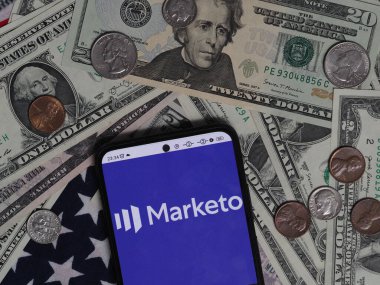 Bavyera, Almanya - 26 Aralık. 2023: Bu resimde Marketo, Inc. logosu, arka planda ABD Doları banknotları ve bozuk paralarla akıllı bir telefonda sergileniyor. Marketo, Adobe A.Ş. 'nin astı.