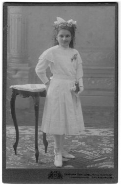 Masanın yanında duran, sol elinde bir kitapla beyaz elbiseli genç bir kızın stüdyo portresi. Fotoğraf stüdyosu Herman Hentschel. Bad Kissingen, Bavyera, Almanya, tarih bilinmiyor, 19. yüzyılın sonları - 20. yüzyılın başları.