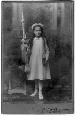 Kafasında çelenk olan beyaz elbiseli, elinde bir kitap ve elinde yanan bir mumla bir masanın yanındaki çantasıyla bir kızın tam boy portresi. Atıcı Walter Klie, Regensburg, Bavyera, Almanya, tarih bilinmiyor, yaklaşık olarak 19.