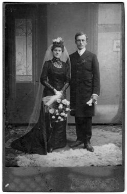 Yeni evlilerin stüdyo boy portresi. Gelinin kafasında bir duvak var ve elinde bir buket beyaz gül tutuyor. Damat uzun bir frak giyiyor ve ellerinde beyaz eldivenler tutuyor. Atıcı Gustav Lang, Regensburg, Bavyera, G