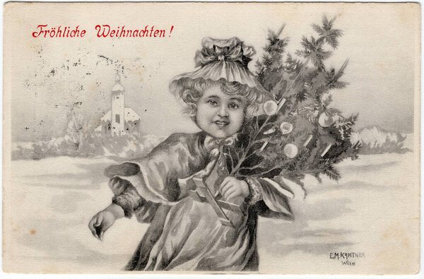 An antique postcard shows a girl holding a Christmas tree against the backdrop of a snow-covered village. Inscription in German: Merry Christmas! Vienna, Austria. Circa 1905