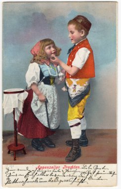 Antika bir kartpostalda stüdyo fotoğrafında geleneksel giysiler içinde bir kız ve bir erkek çocuk görülüyor. Almanca yazıtlar: Apenzeller halk kostümleri. Appenzell, Appenzell-Innerrhoden kantonu, İsviçre. Yaklaşık 1905..