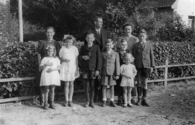 Antika bir fotoğraf beyaz bir adam, iki kadın, bir yaşlı kadın ve altı çocuk gösteriyor, bunlardan üçü kız ve aynı sayıda erkek, arkasında bir evin görülebileceği bir çitin arkasında poz veriyorlar. Almanya. Tarih bilinmiyor, yaklaşık 1930 'larda.