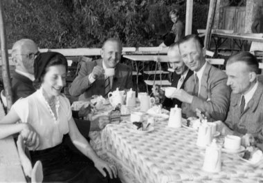 İçinde beş takım elbiseli adamın olduğu antika bir fotoğraf ve verandada kahve içen bir kadın görülüyor. Almanya. Tarih bilinmiyor, yaklaşık 1960 'larda.