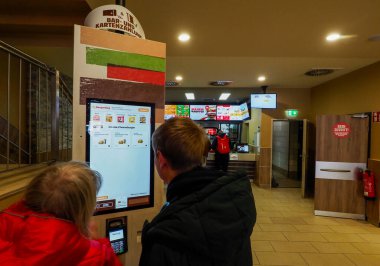 Genç bir adam ve orta yaşlı bir kadın Burger King 'deki sergiye sipariş veriyor.