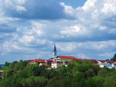 Perlesreut, Gemany - 1 Mayıs 2025: çarpıcı bir gökyüzünün altında ağaçların arasına kurulmuş, önemli bir kilise kulesi olan bir Bavyera kasabası.