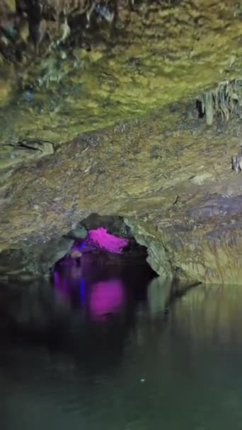 在神秘的五彩斑斓的灯光下 在黑暗的石洞里 在地下河上划船 垂直录像 — 图库视频影像