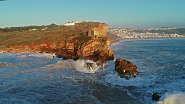 포르투갈 나사레에서 일몰에 파도와 대서양의 해안에 요새와 절벽에 등대의 주위에 — 비디오