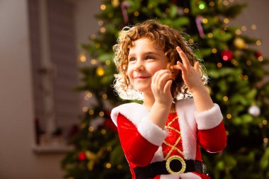 Noel elbisesi içindeki sevimli kız ışıklarla süslenmiş klasik Noel ağacının yanında.