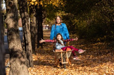 Anne çocukla eğleniyor, balkabaklı bahçe arabası kullanıyor. Sonbahar, şükran zamanı.