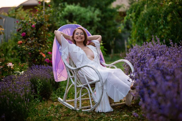 女人穿着花园的白色连衣裙坐在老式椅子上 薰衣草灌木附近松懈的女人 — 图库照片