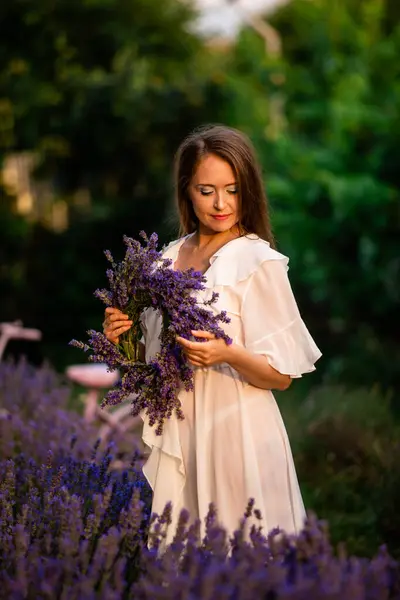Woman with lavender wreath and whitre dress in the garden. Girl collects lavender.