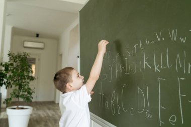 Yeşil karatahtaya ABC harfleri yazan çocuk