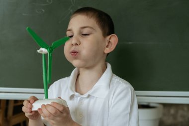 Çocuk rüzgar jeneratörü modelini ve okul tahtasına çizim ve eğitim projesini gösteriyor ve açıklıyor.