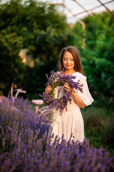 Woman with lavender wreath and whitre dress in the garden. Girl collects lavender.