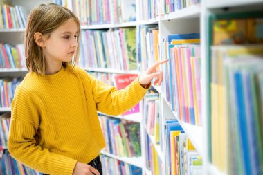 Okul kütüphanesinde kitap seçen liseli kız. Okumak için edebiyat seçen zeki bir kız. Kitapçıdaki raflardaki kitaplar. Kitaplardan öğreniyorum. Okul eğitimi. Günlük okumanın faydaları