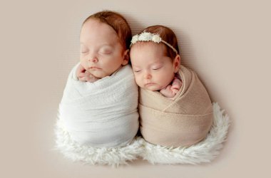 Newborn babies twins swaddled in fabric sleeping on fur. Infant child kids brother and sister studio photoshoot