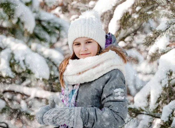 冬の時間には雪の森の中でかなりの子供の女の子のカメラを見て 前ティーン女性子供身に着けている帽子と手袋で寒い天候で雪片 — ストック写真