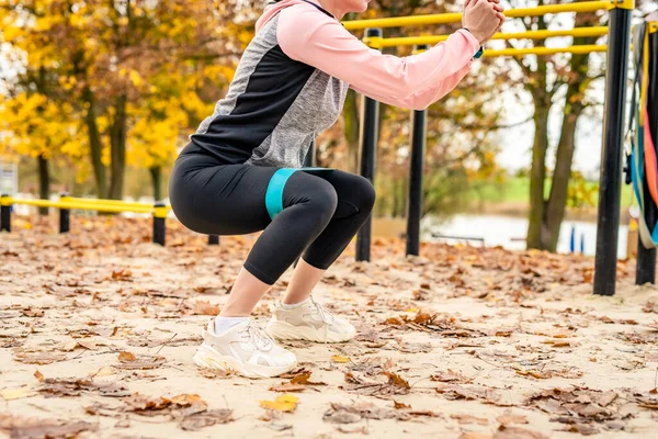 健美的女孩在秋天用橡皮筋做蹲姿 年轻女子在公园运动 腿特写 — 图库照片