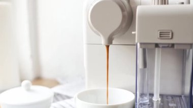 Kahve makinesi beyaz fincanda kapuçino hazırlıyor. Kahvaltıda sıcak kafein içeceği ve fincanda kahve.