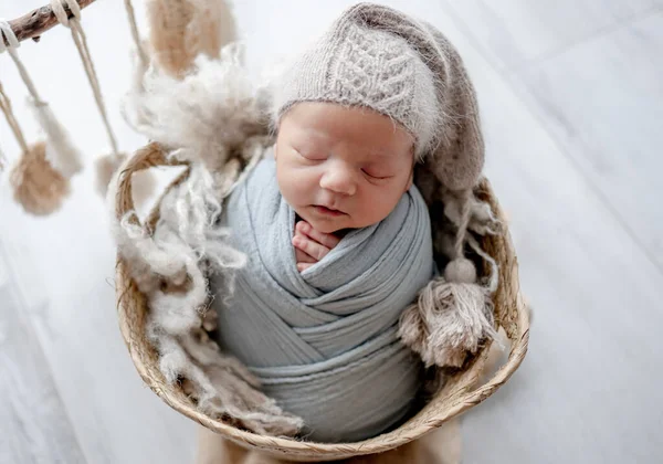 新生児の男の子が生地にはまり込み バスケットスタジオの肖像画で寝て帽子をかぶっていた 乳児期の子供の昼寝 — ストック写真