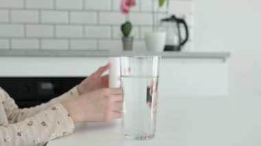 Çocuk eli, köpüklü su bardağında eritmek için pizza hapı koydu. Şeffaf sıvıda aspirin vitamin ilacı