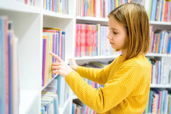 Schoolgirl choosing book in school library. Smart girl selecting literature for reading. Books on shelves in bookstore. Learning from books. School education. Benefits of everyday reading
